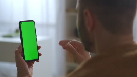 Grüner-Bildschirm-Eines-Modernen-Smartphones-In-Den-Händen-Eines-Mannes,-Der-Per-Videochat-Mit-Freunden-Oder-Kollegen-Chattet,-Nahaufnahme-Des-Gadgets-Durch-Die-Männliche-Schulter
